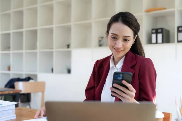 stock image Smiling beautiful Asian businesswoman analyzing chart and graph showing changes on the market and holding smartphone at office..