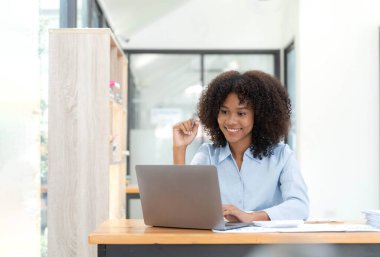 Ev ofisinde online ile bir dizüstü bilgisayar çalışma masasında oturan genç Afrikalı kadın girişimci gülümseyen.