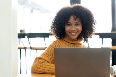 Sarı tişörtlü neşeli, melez bir kadının fotoğrafı laptopta gülümseyen konuşma videosu. Kulaklıklı akıllı etnik kadın evdeki bilgisayarda uzak mesafelere çalışıyor. Eğitim kavramı...