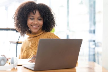 Sarı tişörtlü neşeli, melez bir kadının fotoğrafı laptopta gülümseyen konuşma videosu. Kulaklıklı akıllı etnik kadın evdeki bilgisayarda uzak mesafelere çalışıyor. Eğitim kavramı...
