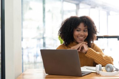 Sarı tişörtlü neşeli, melez bir kadının fotoğrafı laptopta gülümseyen konuşma videosu. Kulaklıklı akıllı etnik kadın evdeki bilgisayarda uzak mesafelere çalışıyor. Eğitim kavramı...