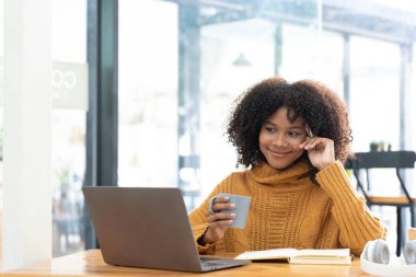 Sarı tişörtlü neşeli, melez bir kadının fotoğrafı laptopta gülümseyen konuşma videosu. Kulaklıklı akıllı etnik kadın evdeki bilgisayarda uzak mesafelere çalışıyor. Eğitim kavramı...