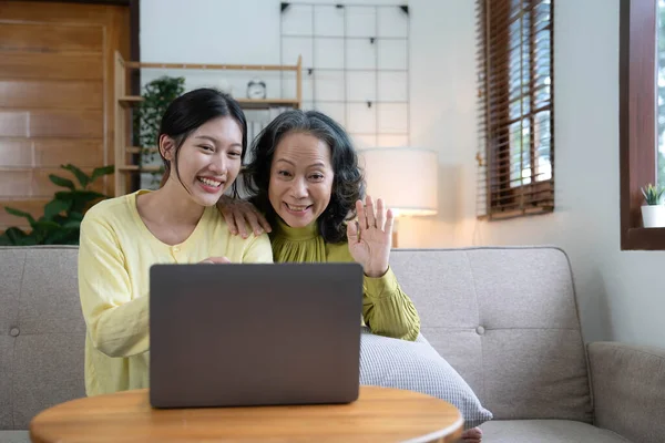 stock image Happy adult granddaughter and senior grandmother having fun enjoying talk sit on sofa in modern living room, smiling old mother hugging young grown daughter bonding chatting relaxing at home together.