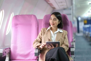 Çekici beyaz kadın uçak yolcusu modern dizüstü bilgisayarda kablosuz bağlantı kullanarak çalışırken rahat koltukta oturuyor.