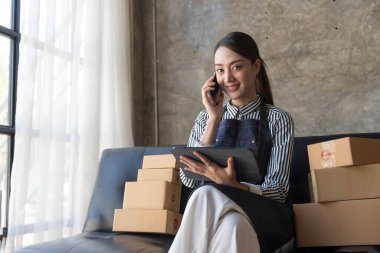 Başlangıçta küçük işletme girişimcisi KOBİ serbest kadın akıllı telefonla çalışıyor, genç Asyalı küçük işletme sahibi bilgisayar kullanıyor, çevrimiçi pazar paketleme kutusu dağıtımı, KOBİ e-ticaret tele pazarlama kavramı..