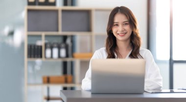 Ofiste çalışan yakışıklı Asyalı kadın dizüstü bilgisayar kullanıyor. Kameraya bakıyor....