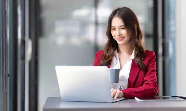 Portrait of smiling beautiful business asian woman in pink suit working in home office desk using computer. Business people employee freelance online marketing e-commerce, work from home concept..