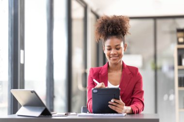 An afro-american young financial assistant businesswoman using digital tablet and laptop while working on financial report...