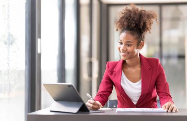 An afro-american young financial assistant businesswoman using digital tablet and laptop while working on financial report...