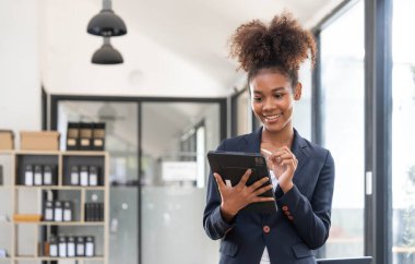 Evdeki ofiste kameraya bakarken dijital tabletini kullanan akıllı afro genç girişimci kadının portresi...