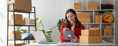 Portrait business woman smile and use tablet checking information on parcel shipping box before send to customer. Entrepreneur small business working at home. SME business online marketing.....