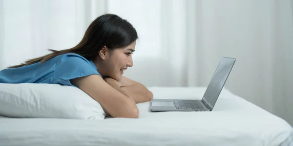Happy, Relaxing Young beautiful Asian female watching movie or series on notebook in emotional smile happily while laying on the bed in her bedroom. Day off, Chill out and leisure concept...
