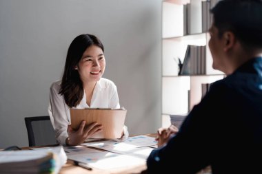 İki iş adamı toplantı odasında proje stratejisi hakkında konuşuyor. İş adamı, mali veri raporu hakkında sohbet ve tavsiyelerde bulunurken, modern işyerindeki iş arkadaşıyla proje planlamasını tartıştı