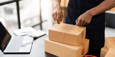 Photo of young entrepreneur man packing he goods while sitting in table comfortable sitting room as background. Shipping, Shopping online, Small business entrepreneur, SME, freelance..