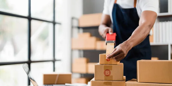 Photo of young entrepreneur man packing he goods while sitting in table comfortable sitting room as background. Shipping, Shopping online, Small business entrepreneur, SME, freelance..