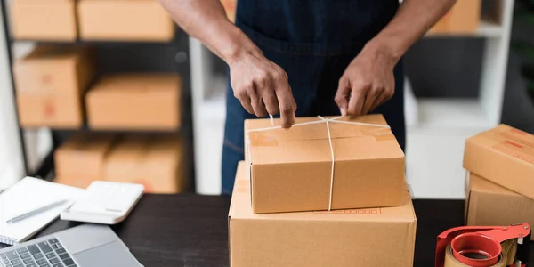 Photo of young entrepreneur man packing he goods while sitting in table comfortable sitting room as background. Shipping, Shopping online, Small business entrepreneur, SME, freelance..