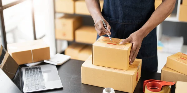 Male online store small business owner entrepreneur seller packing shipping ecommerce box checking website retail order using laptop preparing delivery parcel on table. Dropshipping concept. Closeup.