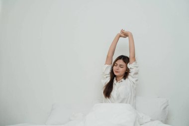 Asian women sitting on bed in the morning after waking up. Young girl on bed in sunny bedroom. Young Girl stretching on bed greets new day with warm sunlight. Beautiful woman stretching on bed...