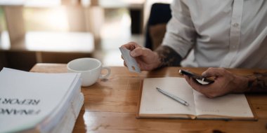 Kredi kartının arkasından bilgi okuyan ve evde online alışveriş yapmak için akıllı telefondan yazan bir adam. Ofisteki bir cep telefonuna online ödeme yapan bir adam...