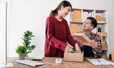 Genç Asyalı çiftler erkek ve kadın küçük işletme sahibi çevrimiçi siparişleri kontrol ediyor ve ürünü birlikte paketliyorlar.