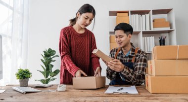 Genç Asyalı çiftler erkek ve kadın küçük işletme sahibi çevrimiçi siparişleri kontrol ediyor ve ürünü birlikte paketliyorlar.
