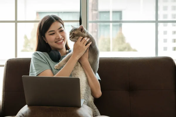 stock image Pretty Asian woman sitting on sofa at home working with laptop in living room smiling happily for today...