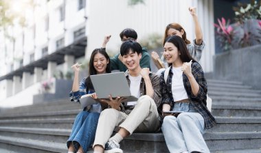 Bir grup neşeli Asyalı üniversite öğrencisi merdivenlerde oturuyor, yumruklarını gösteriyor, zaferi kutluyorlar...