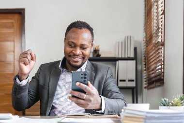 İşte başarı, iyi anlaşma. Afro-Amerikalı adam dizüstü bilgisayara bakıyor, heyecanla bağırıyor ve evde zafer jesti olarak yumruklarını kaldırıyor...