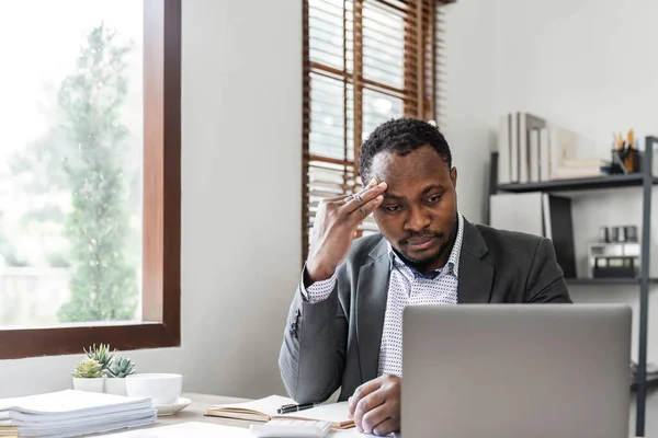 Stressed business man sitting at office workplace. Tired and overworked black man. Young african american exhausted men in stress working on laptop computer..