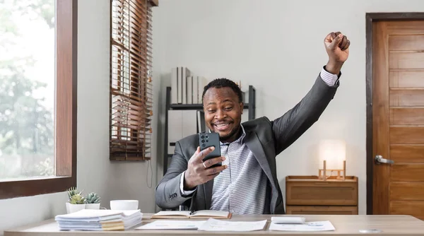 Success at work, good deal. African-American guy looks at the laptop screen, screams excitedly and raises his fists in a victory gesture at home..