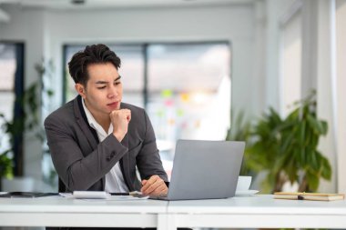 Mutlu milenyum adamı ofis işyerinde dizüstü bilgisayar kullanıyor, evde çalışıyor, iyi haberlerle mesaj okuyor, düşünüyor, ekrana bakıyor, çevrimiçi webinar izliyor, eğitim yapıyor, ödeme yapıyor...