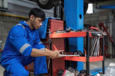 Bir araba servisinde çalışan yakışıklı bir tamircinin portresi çekiliyor. Profesyonel tamirci arabanın altında bir Ratchet kullanır. Modern Temiz Atölye...