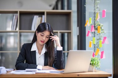 Asyalı iş kadını iş yerinde çok ciddi. Ofiste dizüstü bilgisayarlı belgelerle başağrısı yaratıyor....