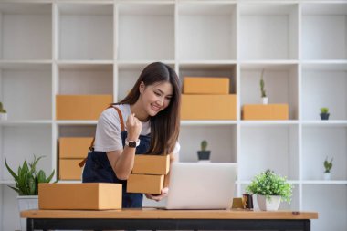 Mutlu Asyalı genç girişimci, internet üzerinden alışveriş merkezinden gelen siparişleri kontrol ettikten sonra satış başarısı için gülümse, internet üzerinden ticaret ve eTicari ticaret kavramı...