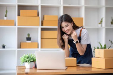 Mutlu Asyalı genç girişimci, internet üzerinden alışveriş merkezinden gelen siparişleri kontrol ettikten sonra satış başarısı için gülümse, internet üzerinden ticaret ve eTicari ticaret kavramı...