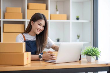Mutlu Asyalı genç girişimci, internet üzerinden alışveriş merkezinden gelen siparişleri kontrol ettikten sonra satış başarısı için gülümse, internet üzerinden ticaret ve eTicari ticaret kavramı...