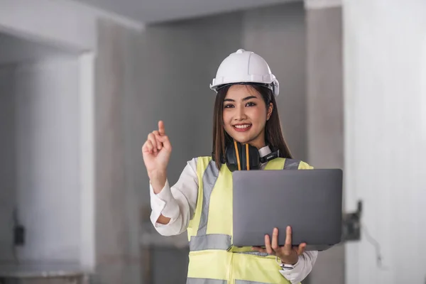 Portrait of Happy professional construction engineer woman holding laptop and wearing the safety helmet at the building site place background, industrial engineering concept..