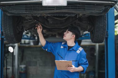 Araç bakımı Asyalı adam garajda araba durumunu kontrol ediyor. Otomotiv tamircisi bakım listesi belgesi. Araba tamir hizmeti kavramı..