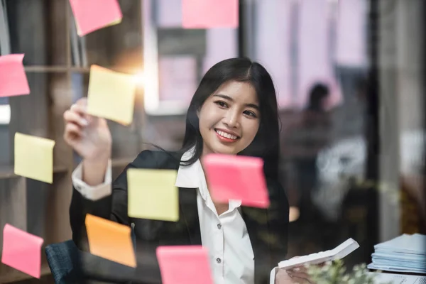 businesswoman write tasks creative ideas and planning on sticky post it note on glass wall.project strategy plan writing target tasks creative ideas on sticky post it notes on glass scrum board office