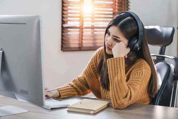 Stock image Tired teen asian lady in headphones falls asleep at table with laptop in room interior. Boring video lesson at home, problems at study, education with modern technology, online webinar and overwork..