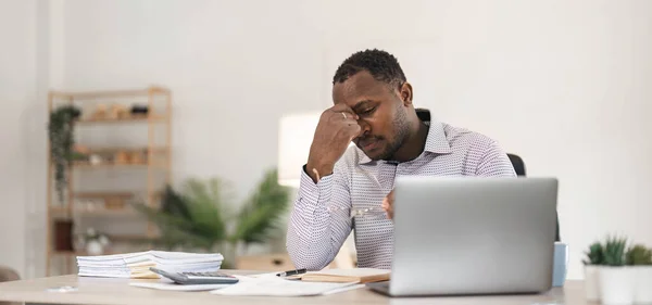Stressed business man sitting at office workplace. Tired and overworked black man. Young african american exhausted men in stress working on laptop computer...