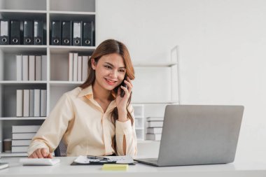 Genç Asyalı iş kadını. Güzel, çekici, gülümseyen ve ofisteki cep telefonunu kullanan....
