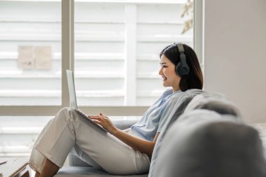 İnternette kulaklık takan genç bir öğrenci, video aracılığıyla sohbet, evdeki kanepede uzaktan öğrenme...