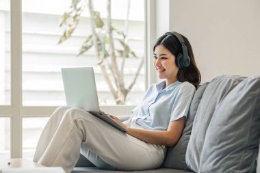 İnternette kulaklık takan genç bir öğrenci, video aracılığıyla sohbet, evdeki kanepede uzaktan öğrenme...