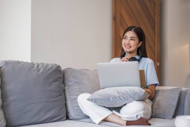 İnternette kulaklık takan genç bir öğrenci, video aracılığıyla sohbet, evdeki kanepede uzaktan öğrenme...