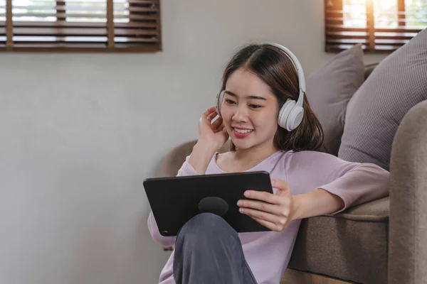 stock image Confident asian woman listening to music with earphones and use tablet while relaxing of work in the office at home...