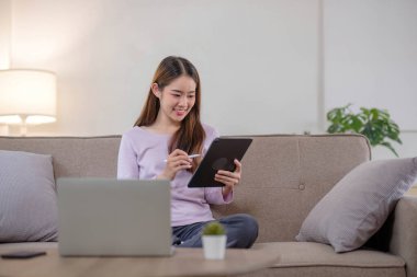 Güzel genç bayan evdeki kanepede otururken dijital tabletini okumak için kullanıyor....