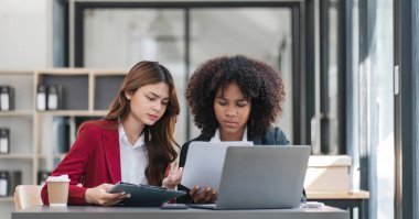 İki iş adamı toplantı odasında proje stratejisi hakkında konuşuyor. İş adamı, mali veri raporu hakkında sohbet ve tavsiyelerde bulunurken, modern işyerindeki iş arkadaşıyla proje planlamasını tartıştı