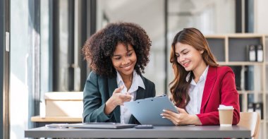 İki iş adamı toplantı odasında proje stratejisi hakkında konuşuyor. İş adamı, mali veri raporu hakkında sohbet ve tavsiyelerde bulunurken, modern işyerindeki iş arkadaşıyla proje planlamasını tartıştı