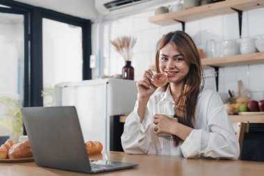 Genç, mutlu, gülümseyen bir kadın, modern mutfakta vegan yemekleri pişirirken dizüstü bilgisayar kullanıyor, gülümseyen hippi kız sağlıklı vitamin salatasını sebzelerle hazırlıyor, sağlıklı yaşam tarzını yiyor...